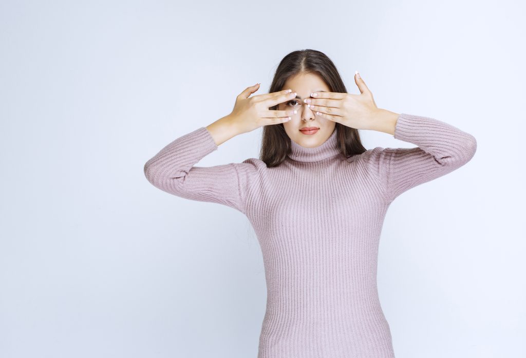 Girl covering one eye and looking with another across her fingers