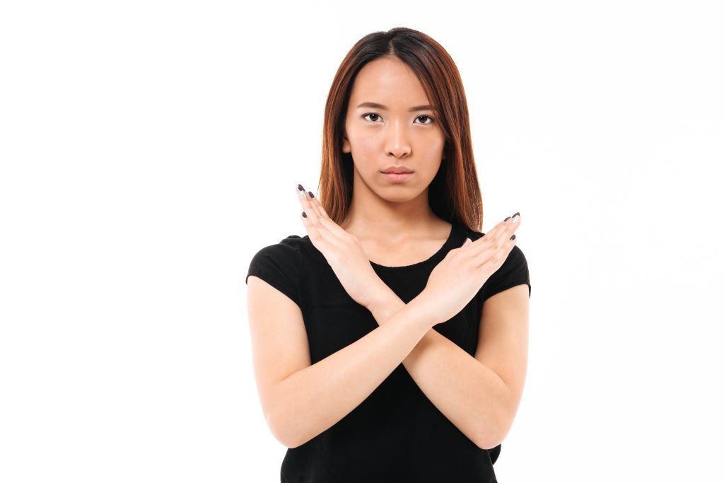 Close-up portrait of serious young asian lady showing stop gestu